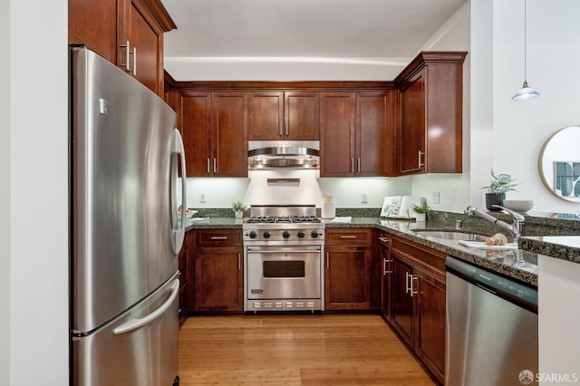 kitchen featuring pendant lighting, light wood finished floors, stainless steel appliances, a sink, and dark stone countertops