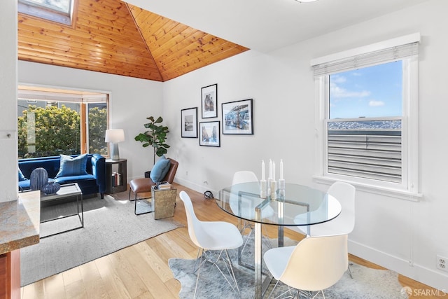 dining area with lofted ceiling with skylight, baseboards, and hardwood / wood-style flooring