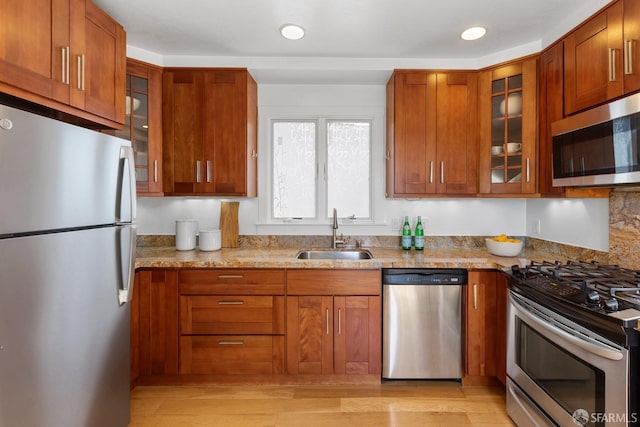 kitchen with a sink, glass insert cabinets, appliances with stainless steel finishes, and brown cabinetry