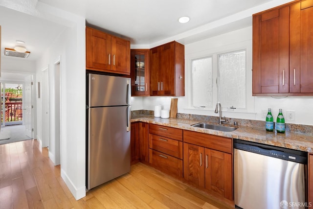 kitchen with visible vents, light wood-style flooring, a sink, stainless steel appliances, and glass insert cabinets