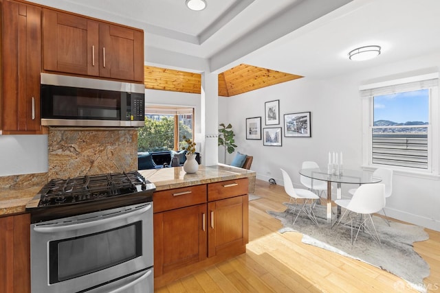 kitchen featuring light wood-style flooring, tasteful backsplash, stainless steel appliances, brown cabinetry, and light countertops