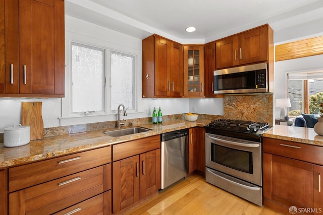 kitchen featuring light stone countertops, light wood finished floors, a sink, stainless steel appliances, and glass insert cabinets