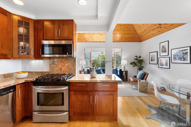 kitchen featuring glass insert cabinets, light stone countertops, light wood-type flooring, a peninsula, and stainless steel appliances