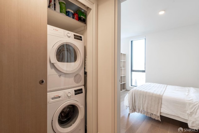 laundry room featuring a wealth of natural light, dark hardwood / wood-style floors, and stacked washer and clothes dryer