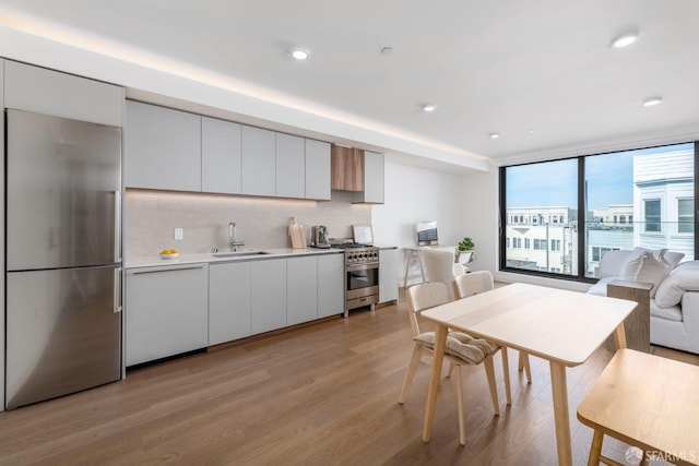 kitchen with decorative backsplash, white cabinets, high end appliances, light wood-type flooring, and sink