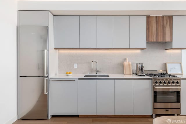 kitchen featuring light wood-type flooring, sink, decorative backsplash, wall chimney exhaust hood, and appliances with stainless steel finishes