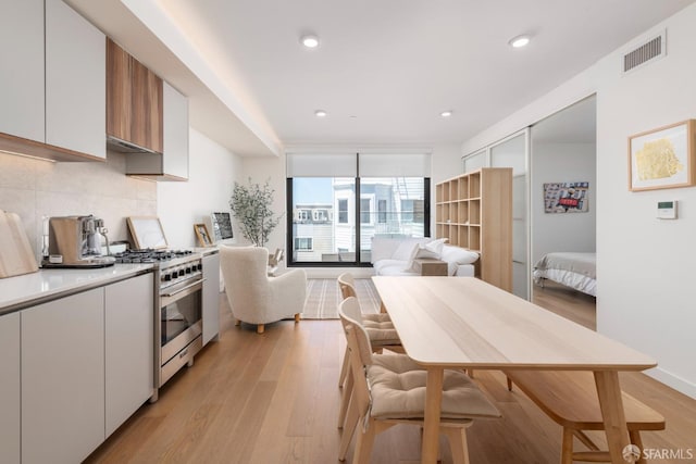 kitchen with white cabinets, light hardwood / wood-style floors, high end stove, and backsplash