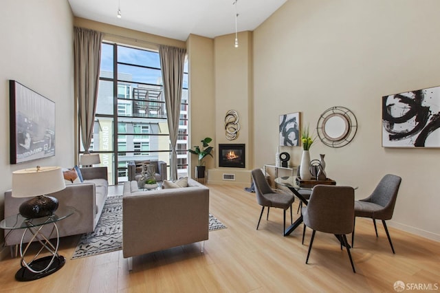 living room with light wood-type flooring, a towering ceiling, and a fireplace