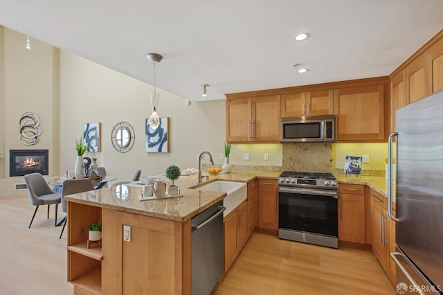 kitchen featuring light stone counters, kitchen peninsula, pendant lighting, stainless steel appliances, and sink