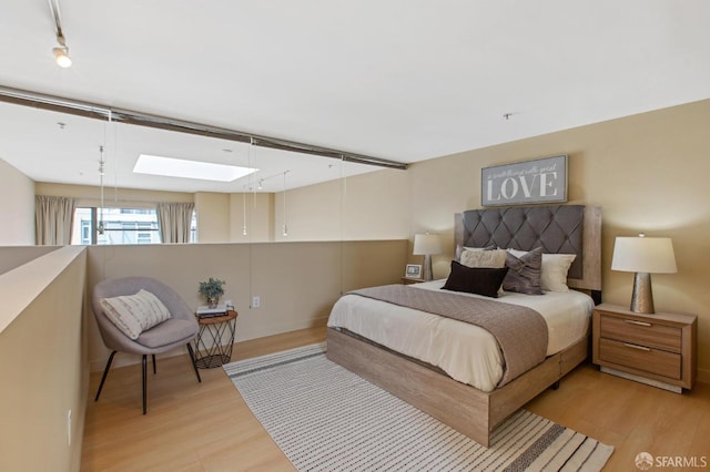 bedroom with light wood-type flooring, rail lighting, and a skylight