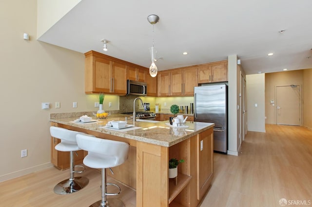 kitchen with appliances with stainless steel finishes, light hardwood / wood-style floors, kitchen peninsula, light stone counters, and decorative light fixtures