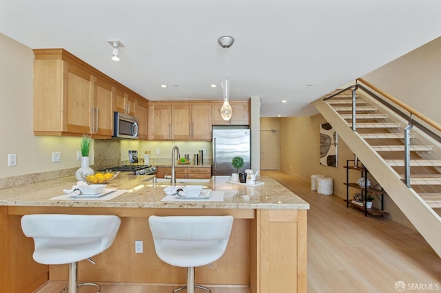 kitchen with stainless steel appliances, sink, light hardwood / wood-style floors, kitchen peninsula, and a breakfast bar