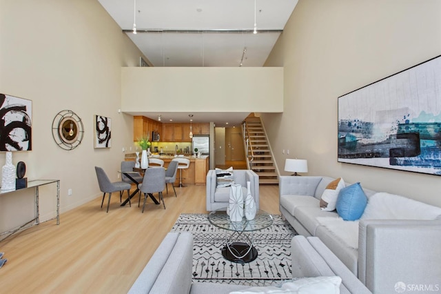 living room with a towering ceiling, rail lighting, and light hardwood / wood-style floors