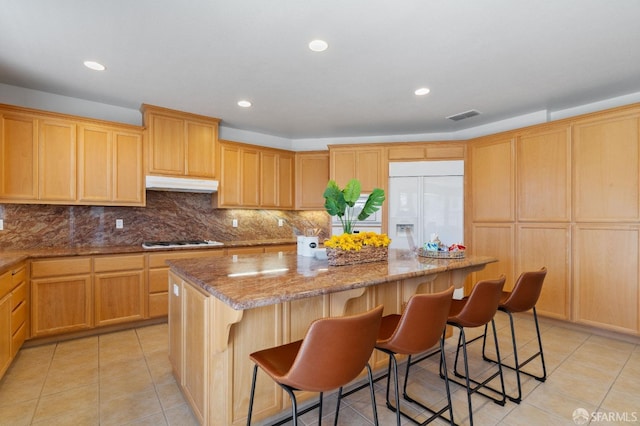 kitchen featuring white refrigerator with ice dispenser, light tile patterned floors, light stone countertops, a center island, and gas cooktop