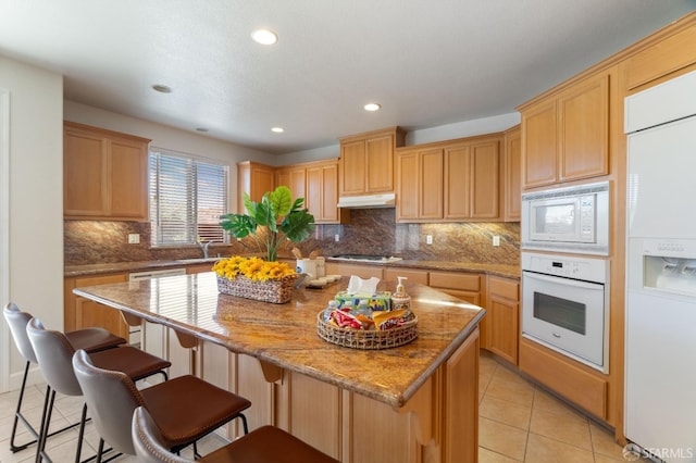 kitchen featuring light stone countertops, white appliances, a kitchen island, sink, and light tile patterned flooring