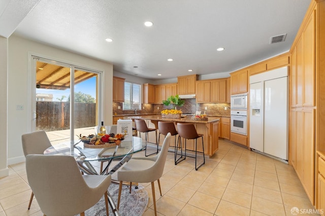 kitchen featuring a kitchen island, built in appliances, backsplash, light tile patterned flooring, and a breakfast bar area