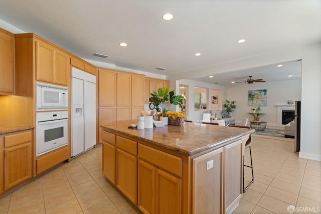 kitchen with a kitchen island, light tile patterned flooring, built in appliances, and stone counters