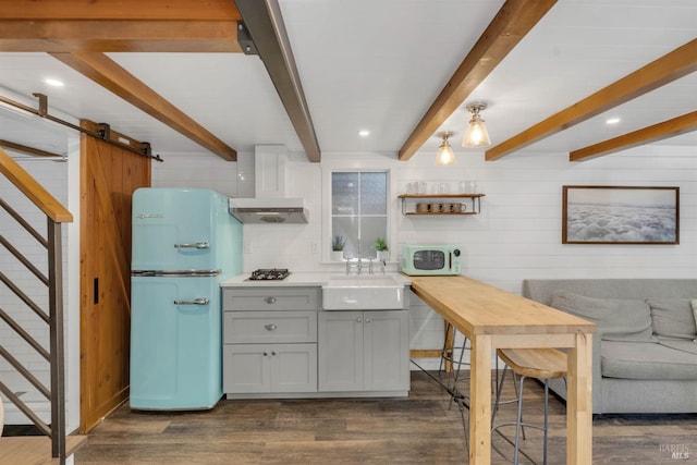 kitchen with white appliances, a barn door, dark wood-style floors, wall chimney exhaust hood, and a sink