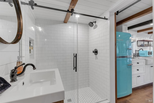 full bath with a shower stall, wood finished floors, a sink, and beamed ceiling