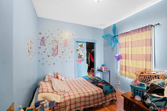 bedroom with a textured ceiling, wood-type flooring, and a closet