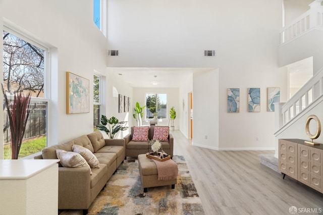 living room with light wood-style floors, visible vents, and a high ceiling