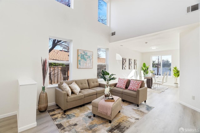 living room featuring light wood-style flooring, a high ceiling, visible vents, and baseboards