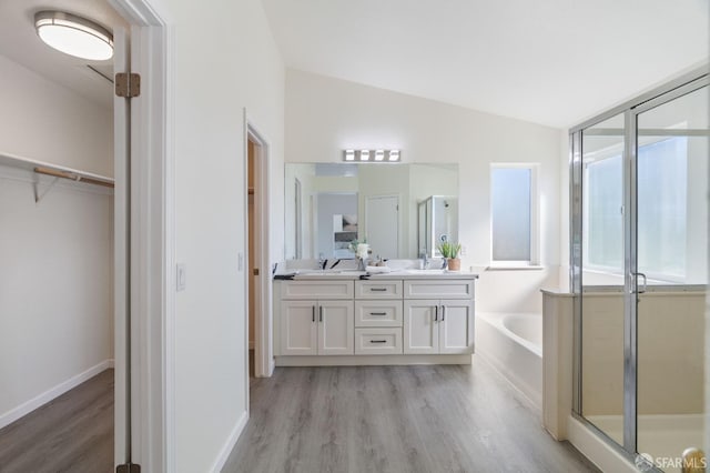 bathroom featuring a stall shower, wood finished floors, a garden tub, vaulted ceiling, and a sink