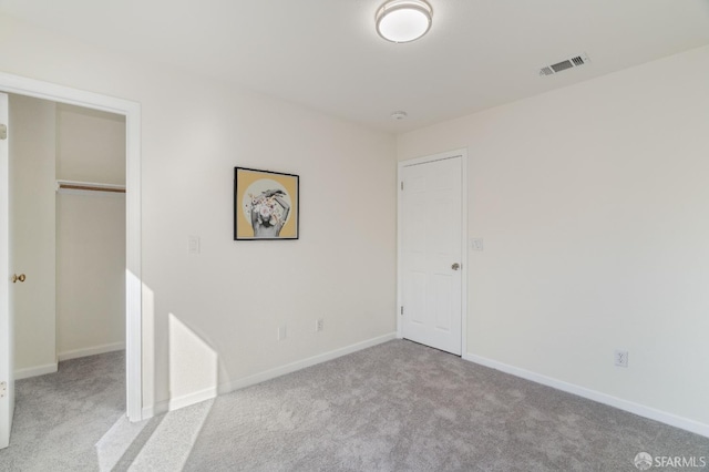 unfurnished bedroom featuring light colored carpet, visible vents, baseboards, a closet, and a walk in closet