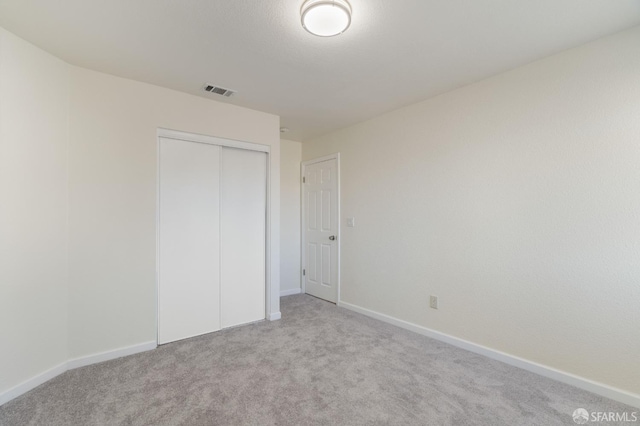 unfurnished bedroom featuring baseboards, a closet, and light colored carpet