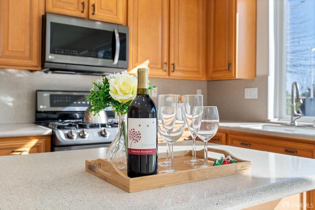 kitchen featuring appliances with stainless steel finishes, brown cabinetry, a sink, and light stone counters