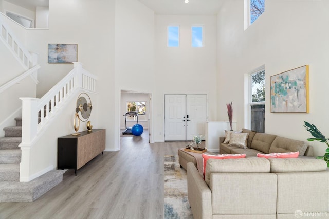 living room featuring baseboards, a healthy amount of sunlight, stairway, and light wood finished floors