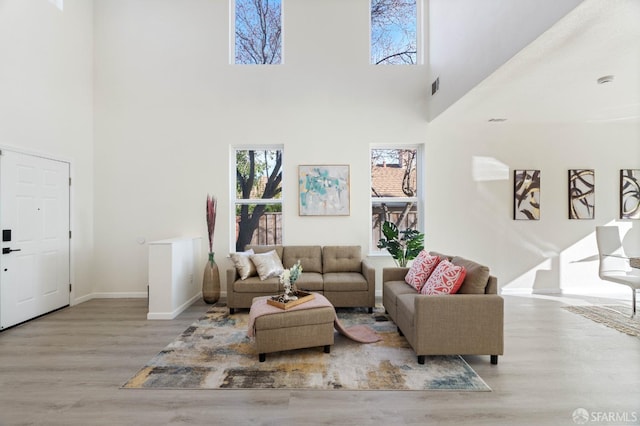 living area with light wood-style floors, a high ceiling, visible vents, and baseboards