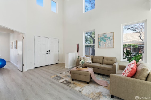 living area with baseboards, a towering ceiling, and light wood finished floors