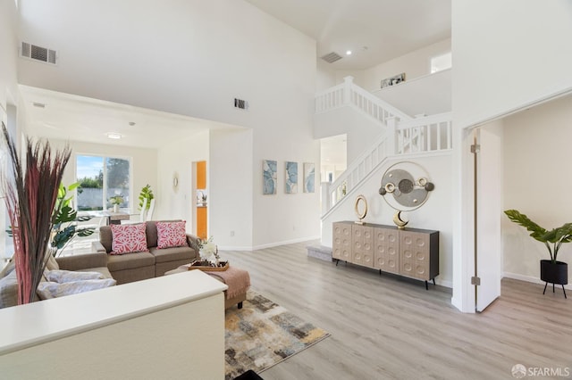 living area featuring baseboards, visible vents, stairway, a high ceiling, and light wood-type flooring