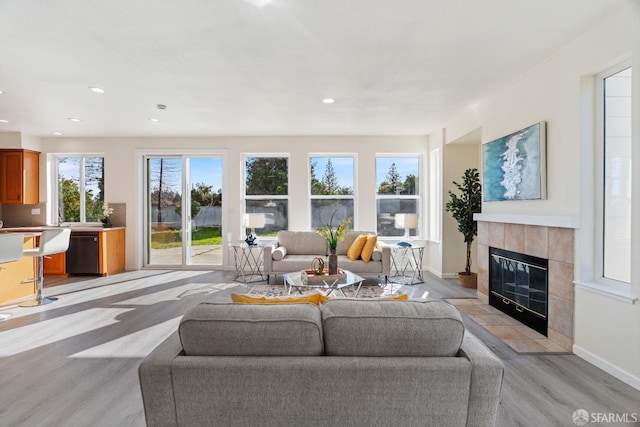 living area featuring a tile fireplace, baseboards, light wood finished floors, and recessed lighting