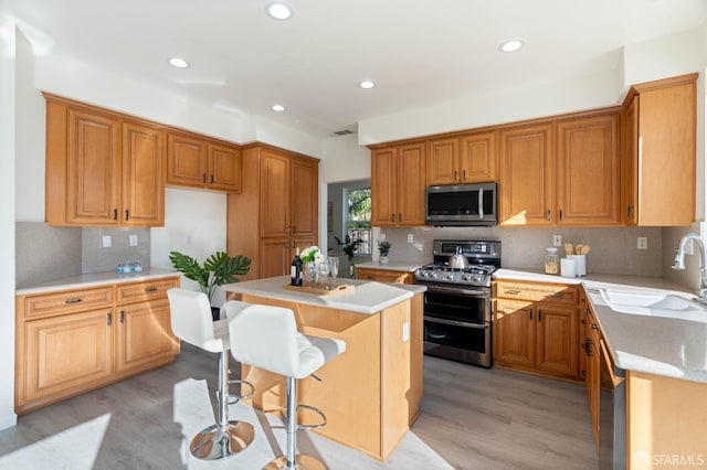 kitchen featuring stainless steel appliances, a sink, a kitchen breakfast bar, light countertops, and a center island