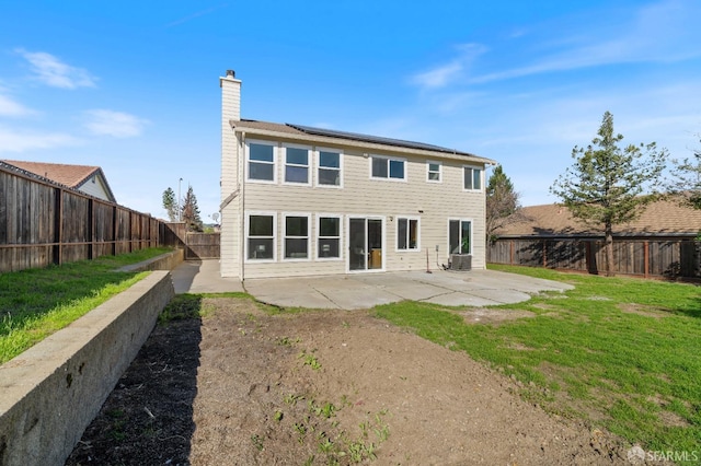 rear view of house featuring a patio, a fenced backyard, a chimney, a yard, and roof mounted solar panels