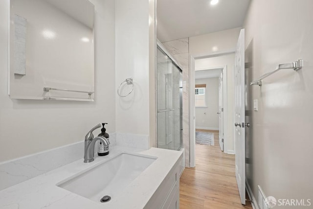 full bath with a shower with door, vanity, baseboards, and wood finished floors