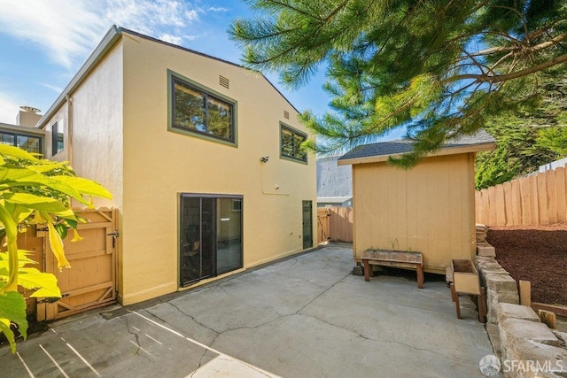 rear view of house with a patio, fence, an outdoor structure, a shed, and stucco siding