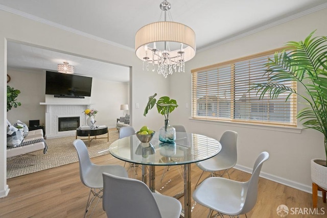 dining area with ornamental molding, wood finished floors, a glass covered fireplace, and a chandelier