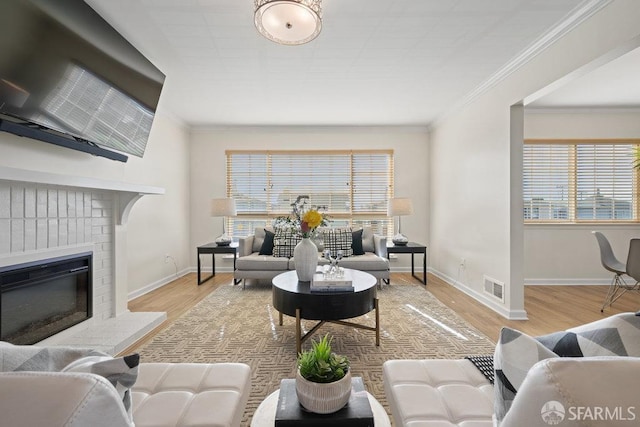 living room featuring wood finished floors, visible vents, baseboards, a brick fireplace, and crown molding