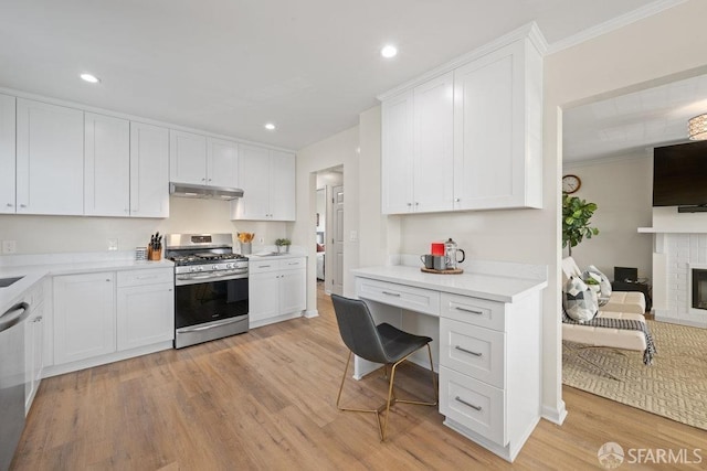 kitchen with under cabinet range hood, a fireplace, white cabinets, appliances with stainless steel finishes, and light wood finished floors