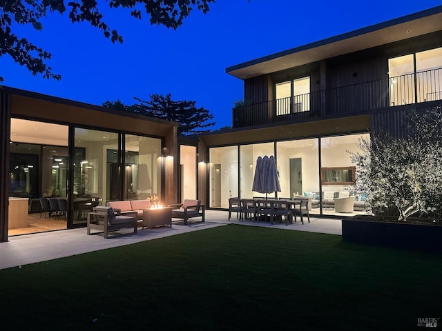 back of house at twilight with an outdoor living space with a fire pit, a yard, a balcony, and a patio