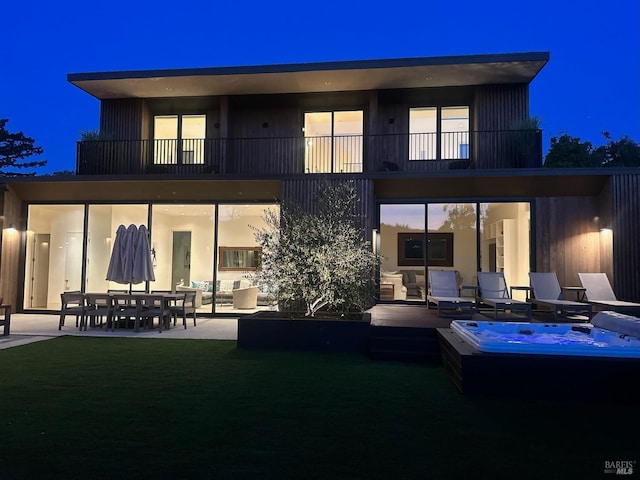 back of house at twilight featuring a balcony, a lawn, and a patio