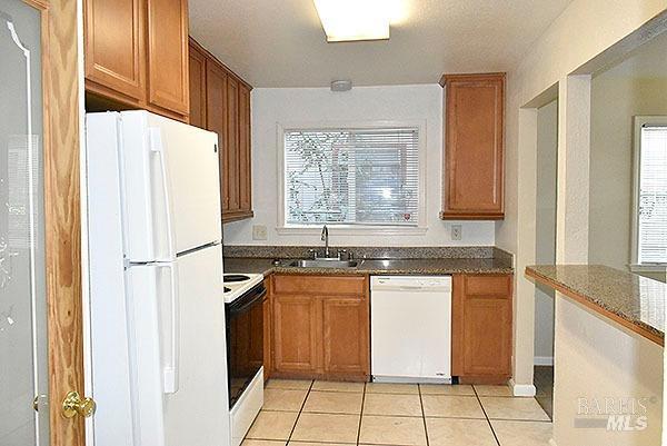 kitchen featuring white appliances, light tile patterned flooring, a healthy amount of sunlight, and a sink