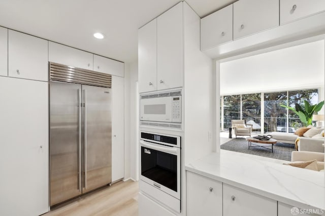 1333 Jones St Unit 508, San Francisco, CA 94109 - kitchen with built in appliances, light stone counters, white cabinetry, light wood-type flooring, and recessed lighting