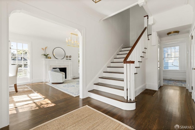 staircase featuring a chandelier, a high end fireplace, baseboards, and wood finished floors