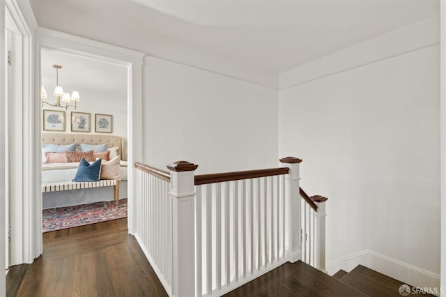 corridor with baseboards, wood finished floors, an upstairs landing, and a notable chandelier