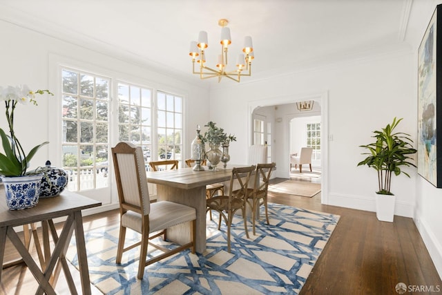 dining space featuring arched walkways, crown molding, wood finished floors, baseboards, and an inviting chandelier