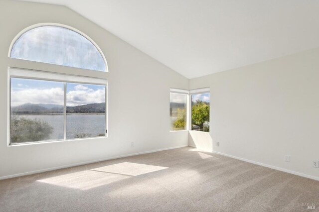 carpeted spare room with baseboards, a water view, and high vaulted ceiling